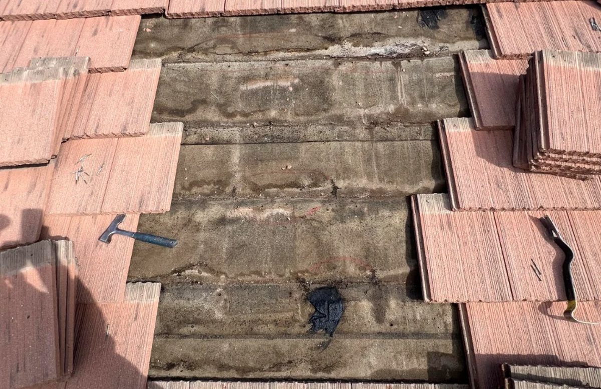 Concrete tile lifted on an Arizona roof, exposing aged underlayment and old patch repairs underneath