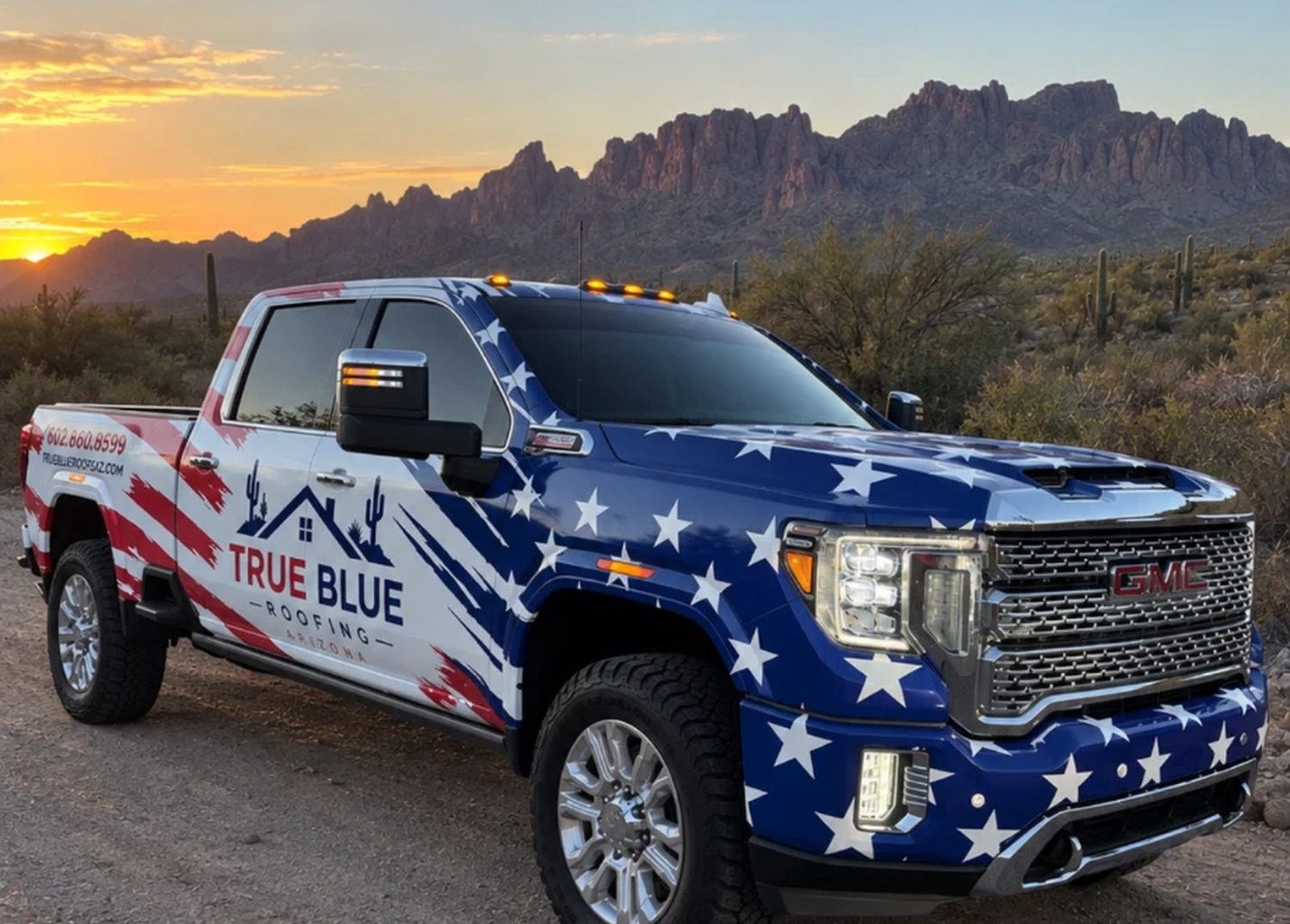 The True Blue Roofing Arizona truck, wrapped in the stars and stripes, parked in the desert below the Superstition Mountains at sunset